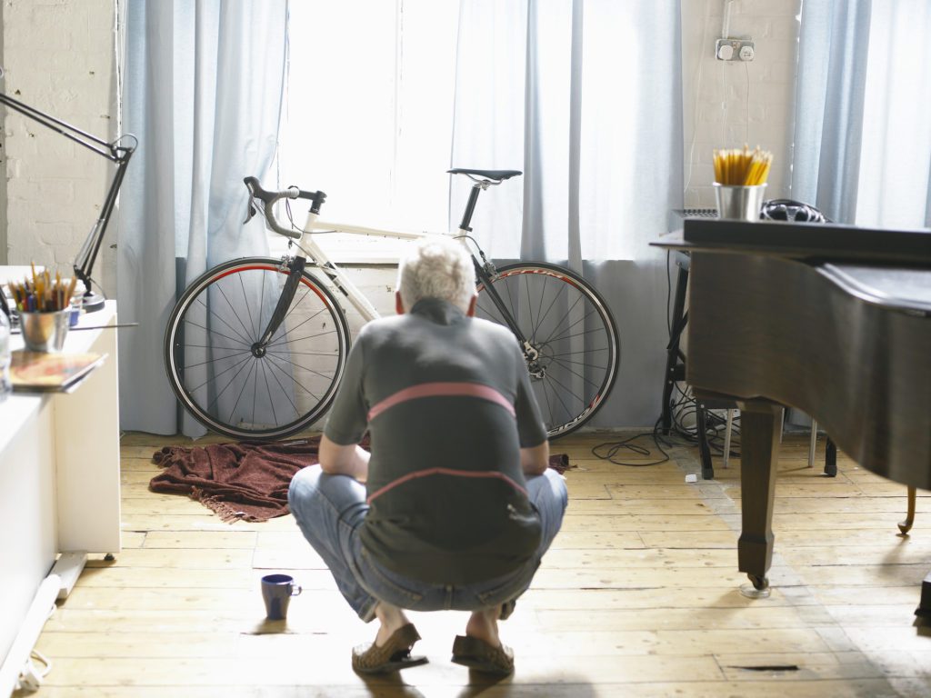 Mature man crouching down, looking at bicycle, rear view