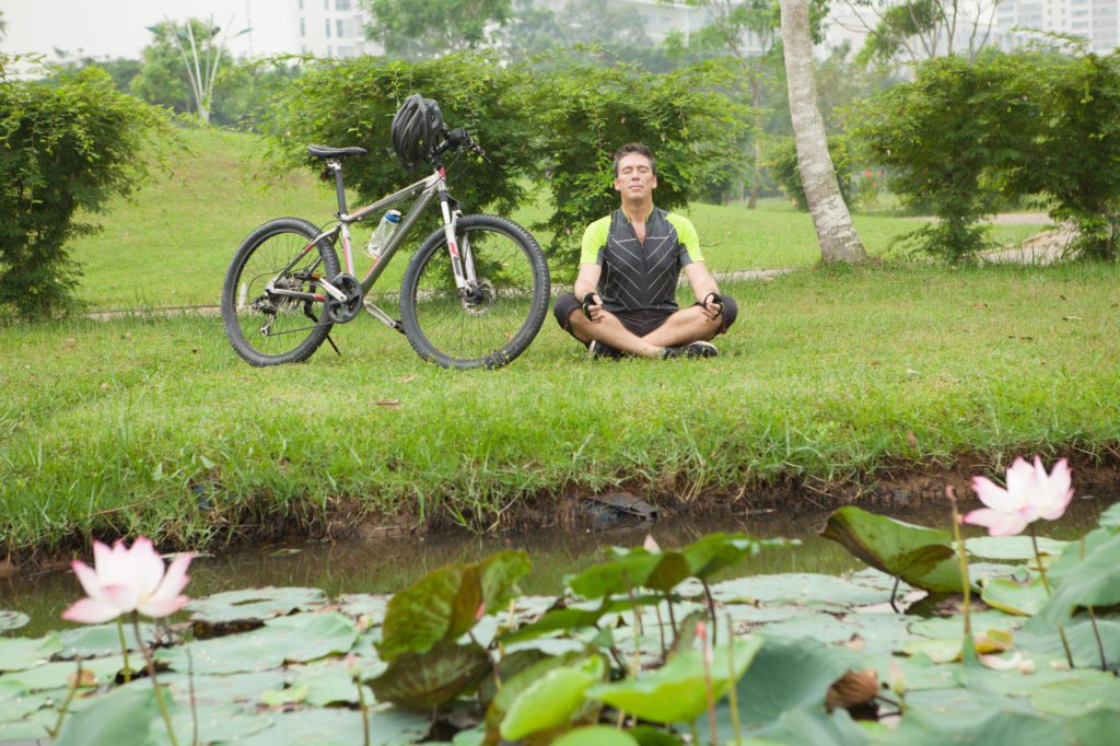 Close up image of a relaxed cyclist sitting in lotus posture near the bicycle on the foreground