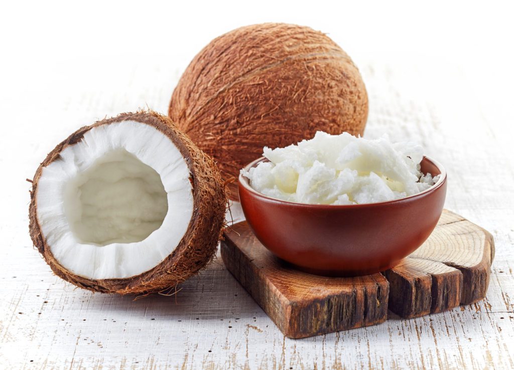 bowl of coconut oil and fresh coconuts on white wooden table