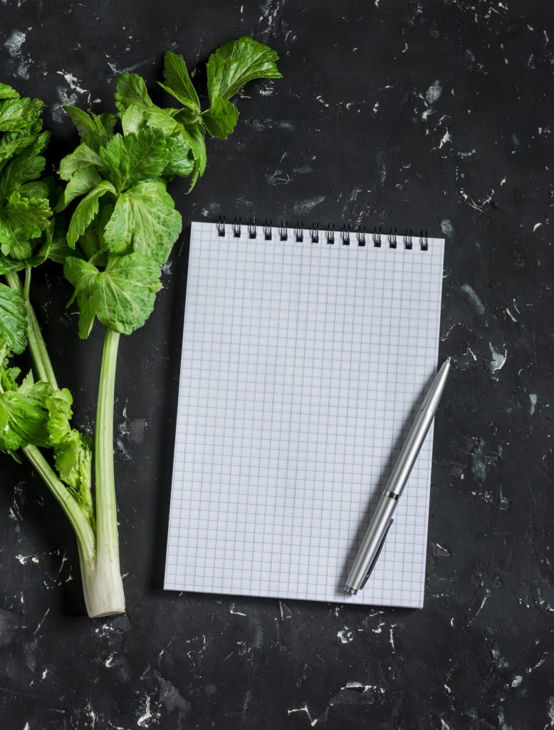 Clean blank notepad and a branch of fresh celery on a dark background. Concept of diet, planning and healthy lifestyle