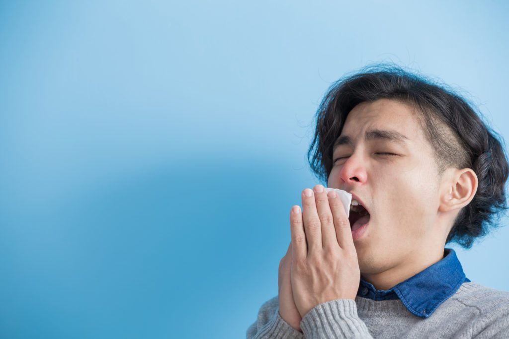 man is sick and sneezing with blue background, asian