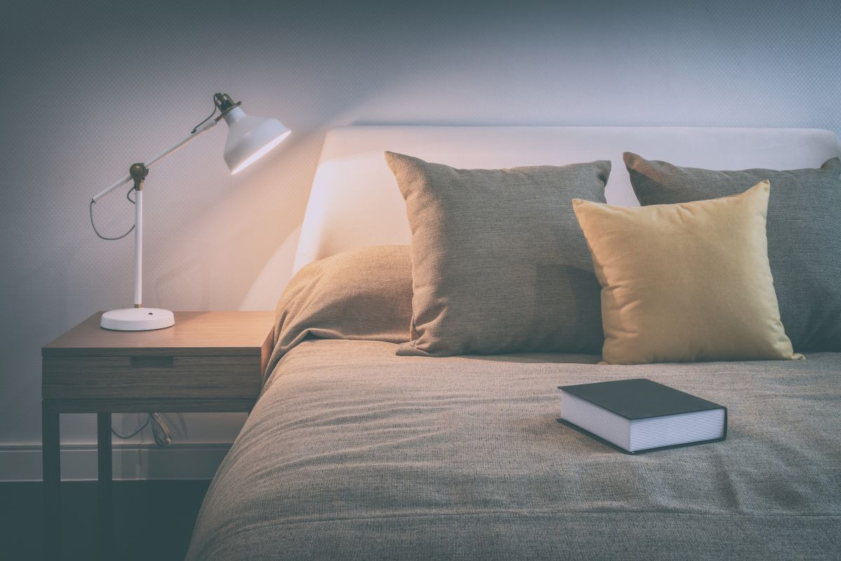 vintage style photo of cozy bedroom interior with book and reading lamp on bedside table