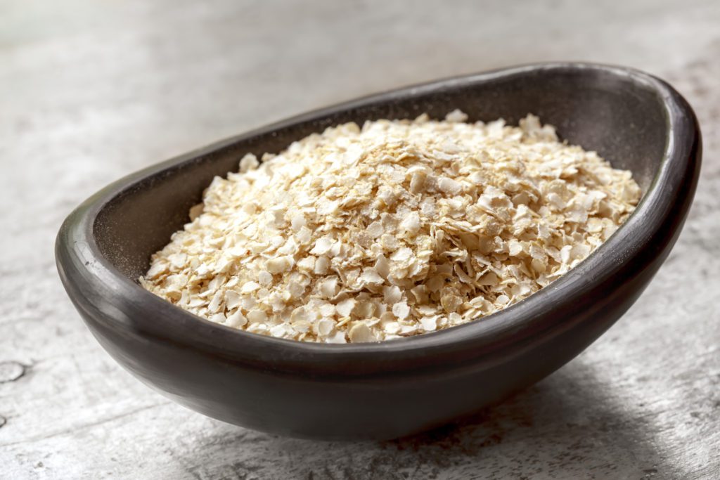 Quinoa flakes in small black bowl over rustic wood.