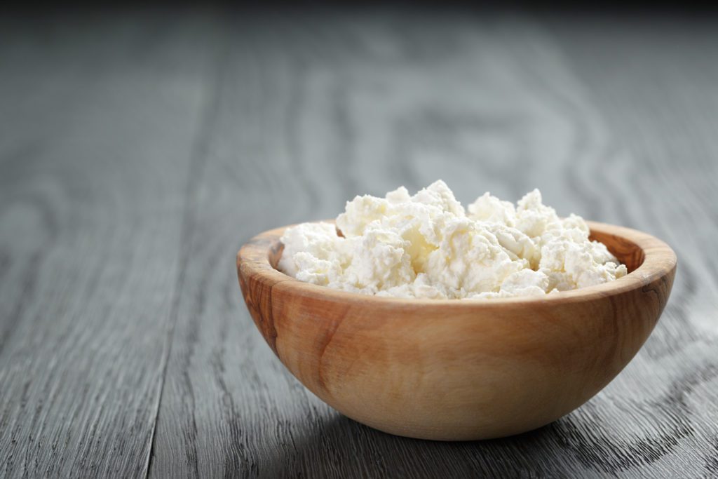 fresh ricotta in olive wood bowl on old table, shallow focus