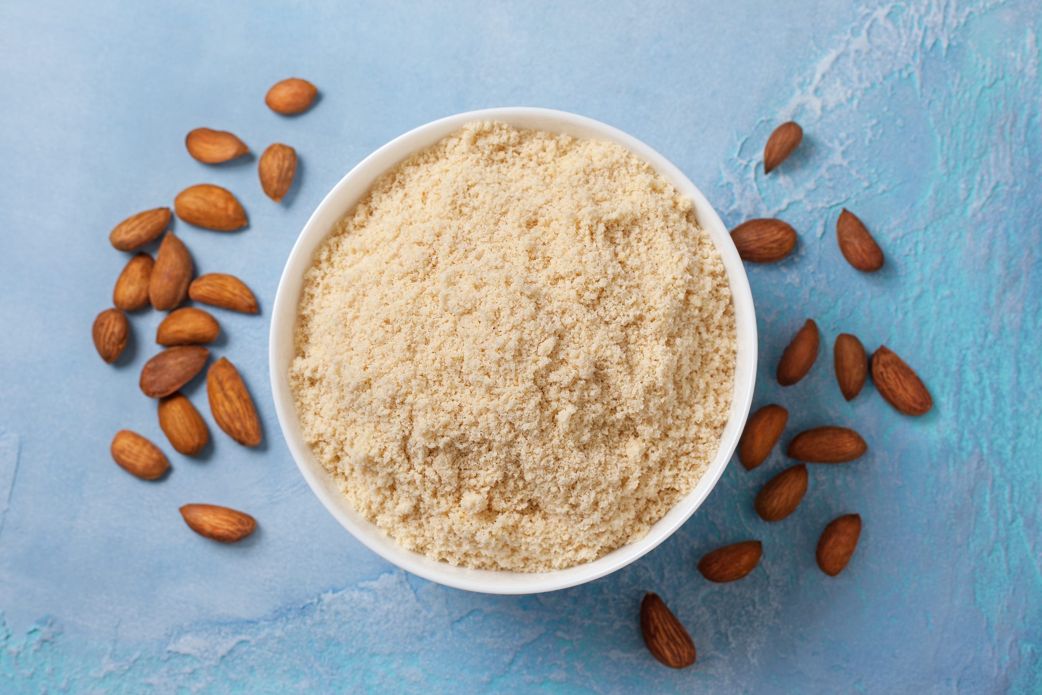 almond  flour in a white bowl, almonds on a blue background ( view from above)"