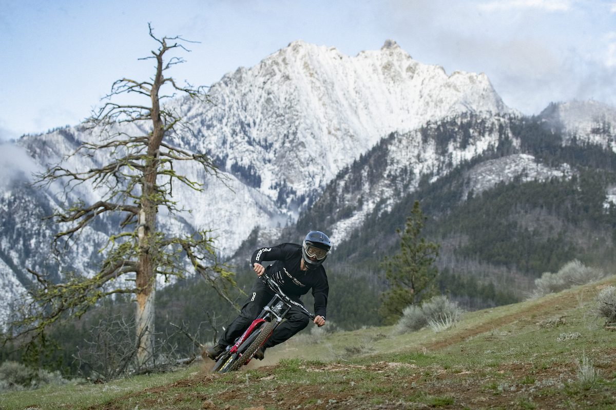 Elliot Jamieson corners his mountain bike below a snow-covered mountian peak 