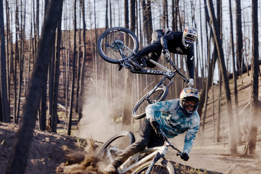 Two riders jump through a fire charred forest  