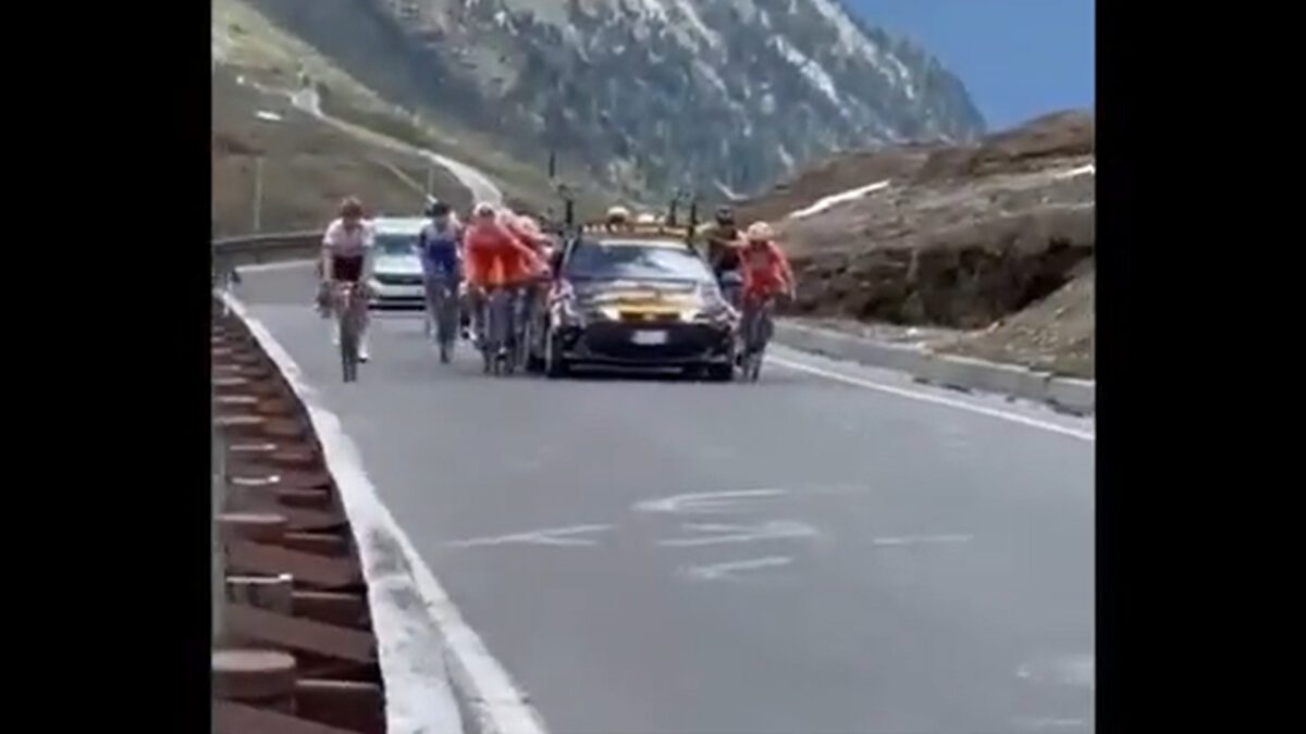 Riders hold onto cars during the Giro Next Gen