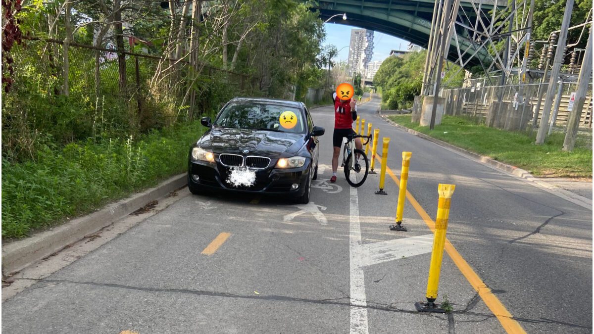 A cyclist in a bike lane where there is a car in Toronto