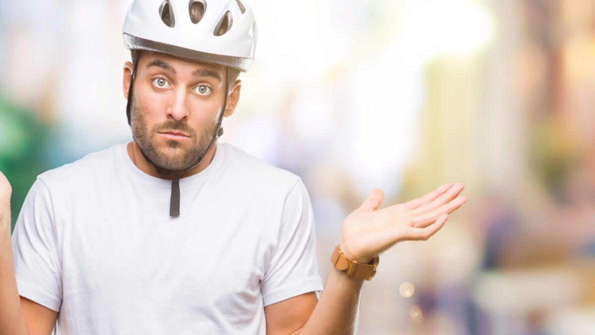 Young handsome man wearing cyclist safety helmet over isolated background clueless and confused expression with arms and hands raised. Doubt concept.