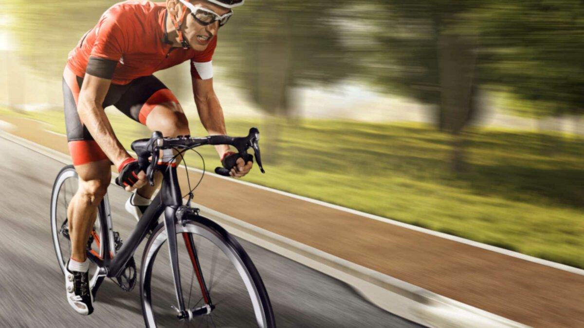 An athlete is riding a bicycle on a spiral track. The man is wearing black bike shorts and shin guards along with a red sleeveless top and a red and white helmet and sunglasses. With intentional lens flare and high speed motion blur.